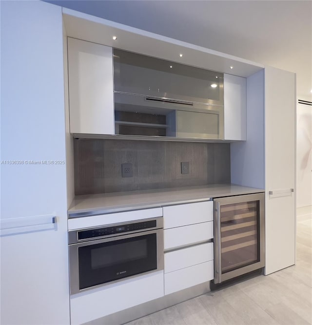 kitchen featuring wine cooler, white cabinetry, light hardwood / wood-style flooring, and oven