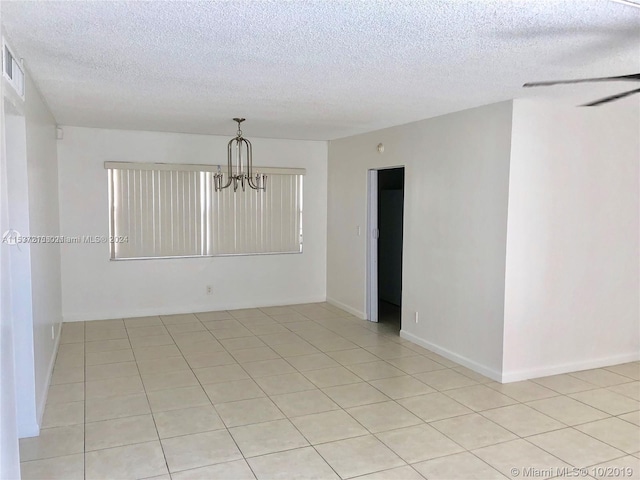 tiled spare room featuring a textured ceiling and ceiling fan with notable chandelier