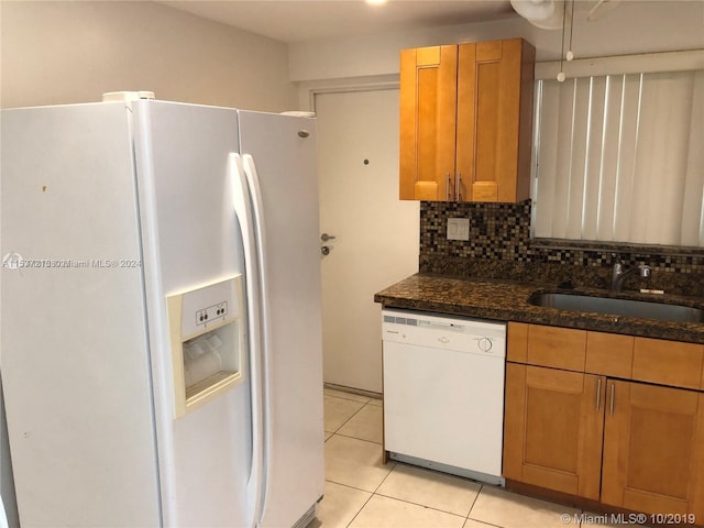 kitchen featuring backsplash, light tile flooring, white appliances, sink, and dark stone countertops