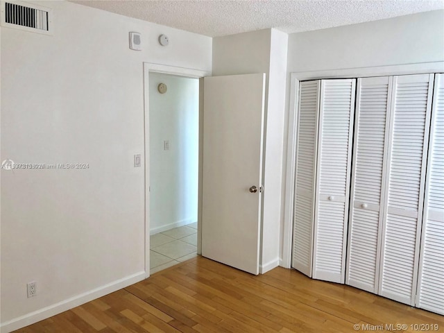 unfurnished bedroom with light hardwood / wood-style floors, a textured ceiling, and a closet