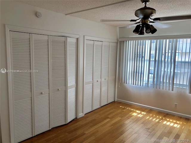 unfurnished bedroom featuring multiple windows, light hardwood / wood-style floors, two closets, and a textured ceiling