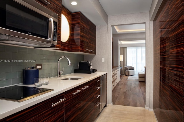 kitchen with tasteful backsplash, sink, black electric stovetop, and light hardwood / wood-style flooring