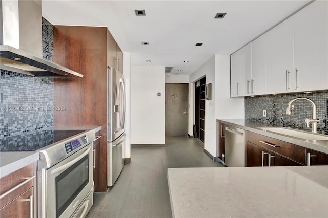 kitchen featuring appliances with stainless steel finishes, sink, white cabinets, wall chimney range hood, and tasteful backsplash