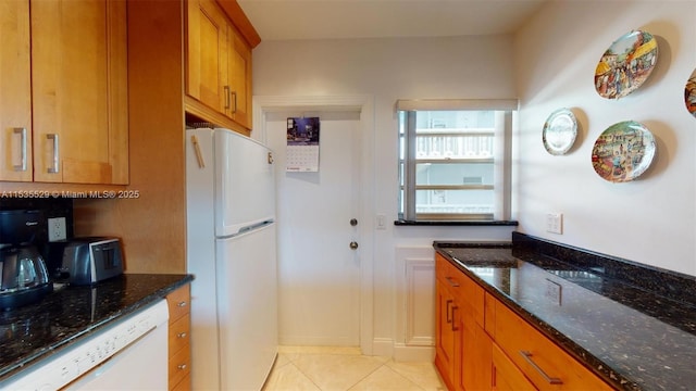 kitchen with light tile patterned flooring, white appliances, and dark stone countertops