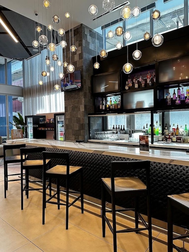 bar with decorative light fixtures, light tile floors, and a towering ceiling