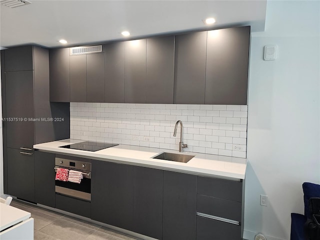 kitchen featuring light tile floors, tasteful backsplash, black electric stovetop, oven, and sink