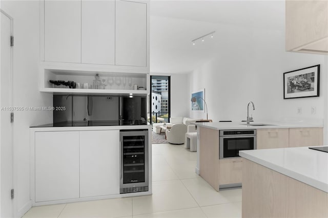 kitchen with light tile patterned floors, modern cabinets, wine cooler, stainless steel oven, and a sink