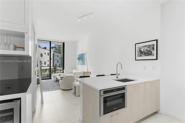 kitchen featuring oven, a peninsula, a sink, expansive windows, and track lighting