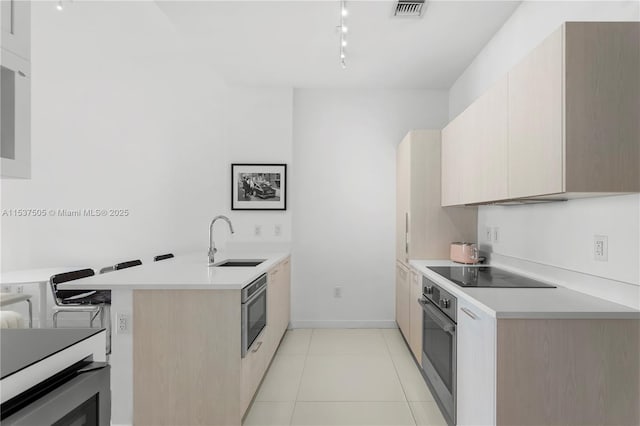 kitchen with black electric stovetop, oven, a peninsula, a sink, and visible vents