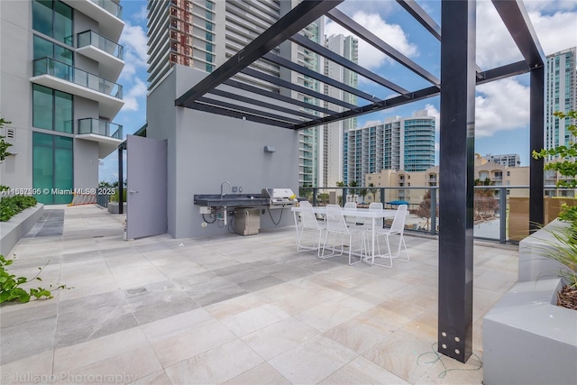 view of patio featuring outdoor dining area, an outdoor kitchen, a city view, a grill, and a pergola