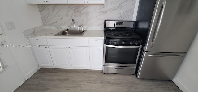 kitchen featuring appliances with stainless steel finishes, white cabinets, hardwood / wood-style floors, sink, and decorative backsplash