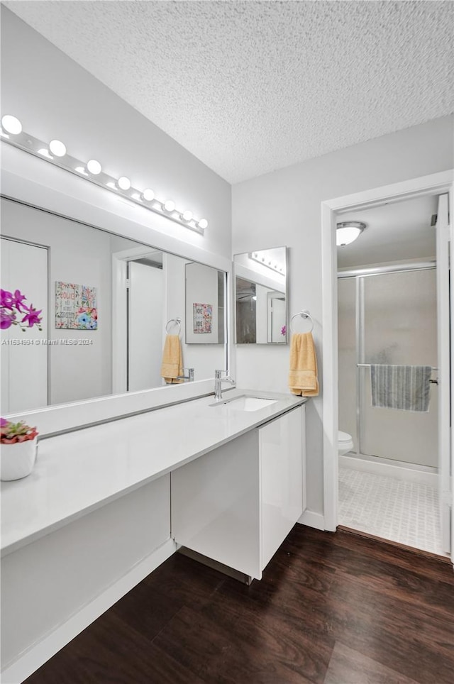 bathroom with a textured ceiling, wood-type flooring, vanity with extensive cabinet space, and toilet