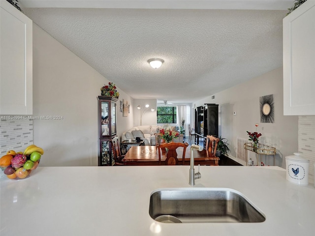 kitchen with a textured ceiling, backsplash, sink, and white cabinetry