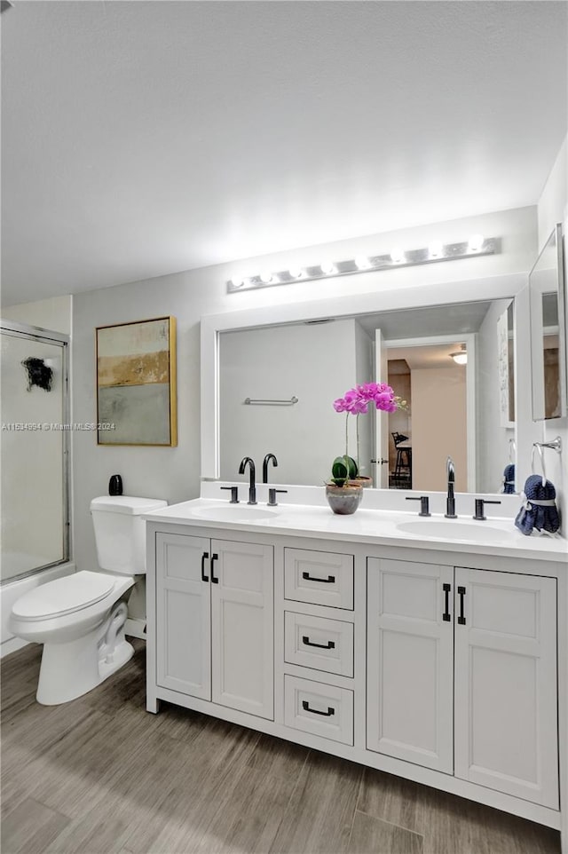 full bathroom with dual sinks, toilet, shower / bath combination with glass door, large vanity, and hardwood / wood-style flooring