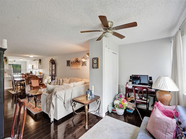 living room with a textured ceiling, ceiling fan, and dark wood-type flooring