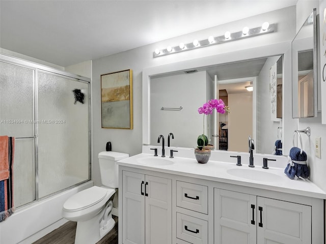 full bathroom with dual vanity, shower / bath combination with glass door, toilet, and hardwood / wood-style floors