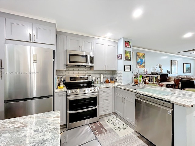 kitchen featuring kitchen peninsula, appliances with stainless steel finishes, sink, and light stone countertops