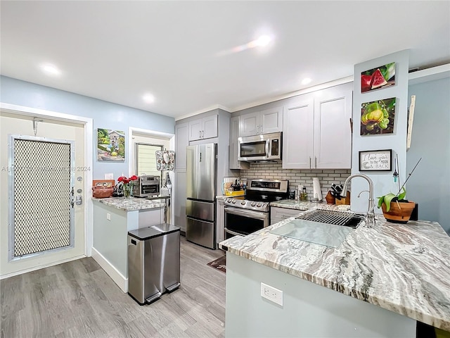 kitchen with stainless steel appliances, kitchen peninsula, sink, light stone countertops, and light wood-type flooring