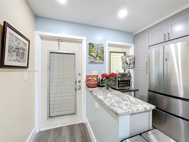 kitchen featuring hardwood / wood-style floors, gray cabinetry, stainless steel refrigerator, and light stone countertops