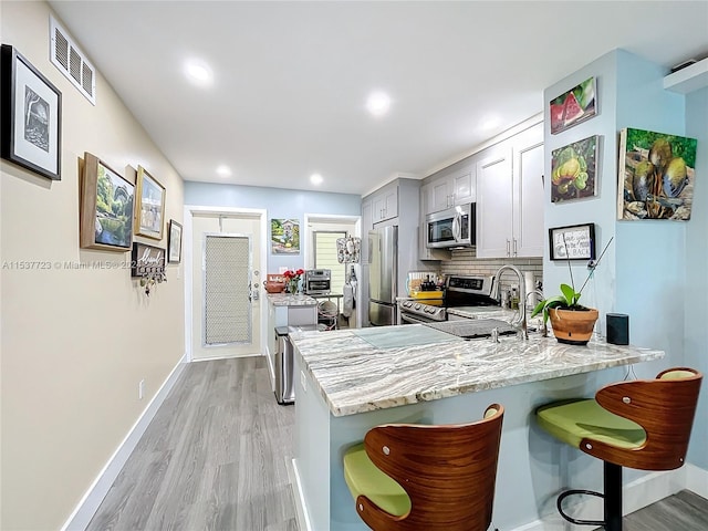 kitchen featuring stainless steel appliances, kitchen peninsula, decorative backsplash, gray cabinetry, and light hardwood / wood-style flooring