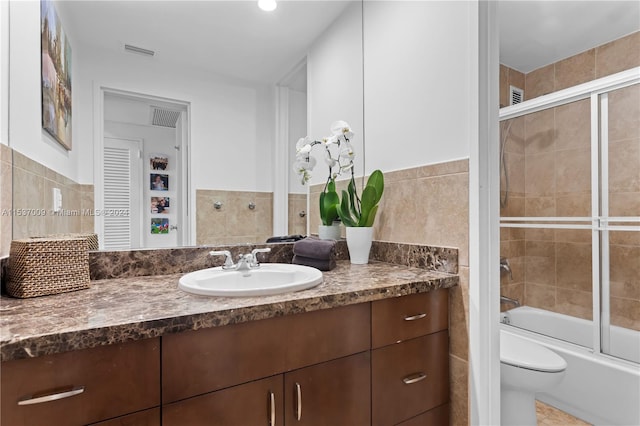 full bathroom featuring toilet, vanity, tile walls, tile flooring, and bath / shower combo with glass door