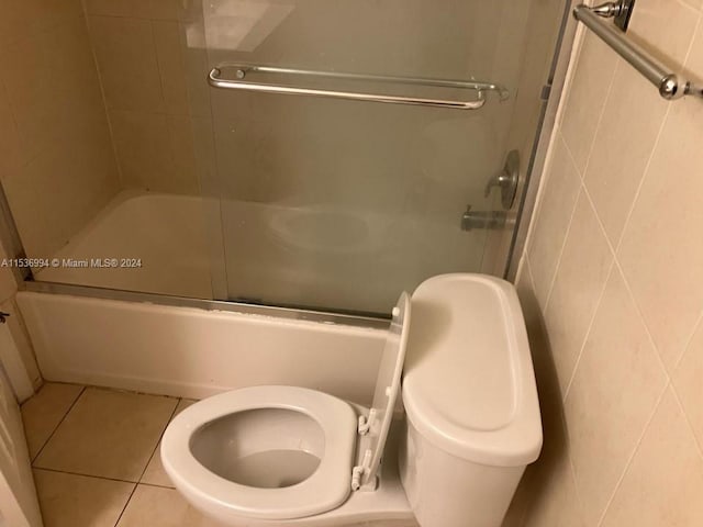 bathroom featuring tile walls, combined bath / shower with glass door, toilet, and tile floors