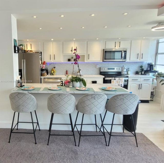 kitchen with white cabinetry, backsplash, light hardwood / wood-style flooring, stainless steel appliances, and a breakfast bar area