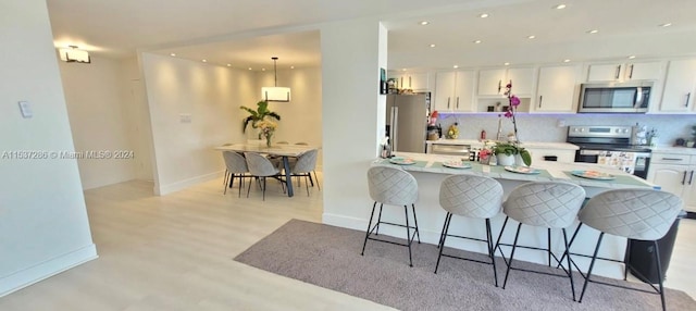 kitchen featuring a kitchen breakfast bar, white cabinets, tasteful backsplash, and stainless steel appliances