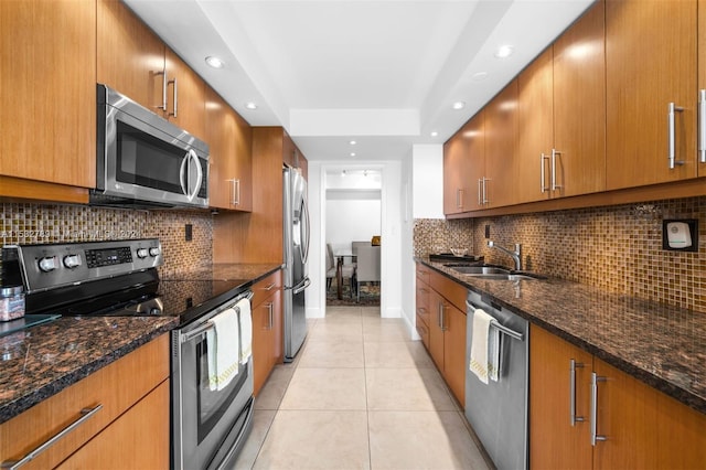 kitchen featuring backsplash, light tile flooring, sink, stainless steel appliances, and dark stone counters