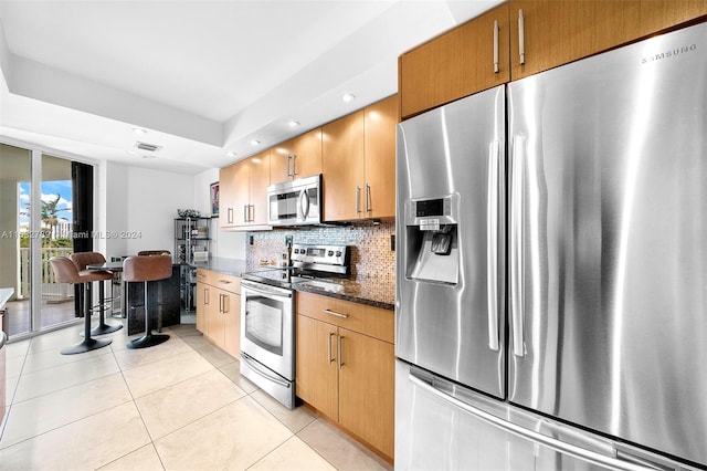 kitchen featuring dark stone counters, tasteful backsplash, stainless steel appliances, and light tile floors