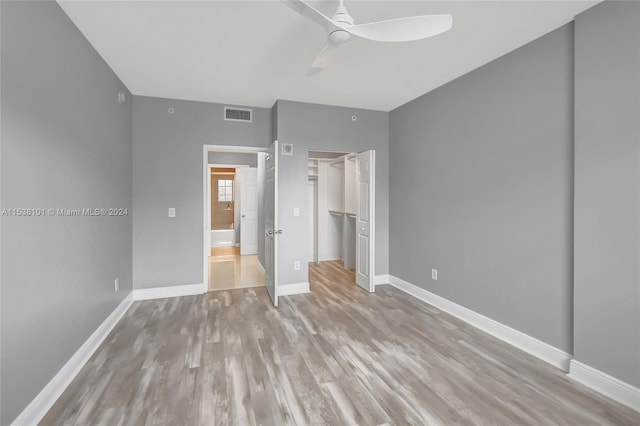 unfurnished bedroom featuring a walk in closet, a closet, ceiling fan, and light wood-type flooring