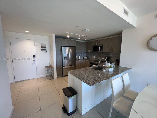 kitchen with visible vents, a peninsula, dark stone counters, stainless steel appliances, and decorative backsplash