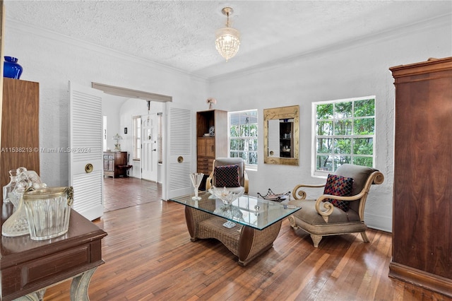 living room featuring a notable chandelier, wood-type flooring, a textured ceiling, and ornamental molding