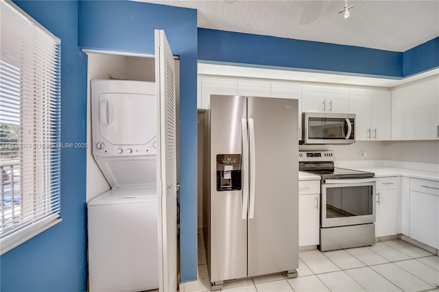 kitchen with white cabinetry, stacked washer / drying machine, light tile patterned floors, stainless steel appliances, and a textured ceiling