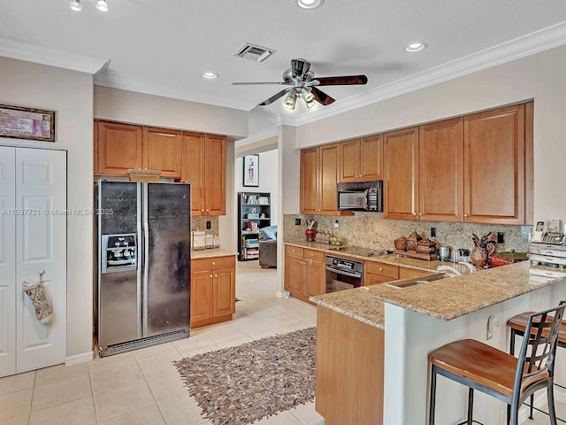 kitchen featuring light stone counters, a kitchen breakfast bar, a peninsula, black appliances, and a sink