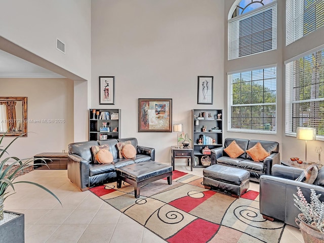 living area featuring ornamental molding, visible vents, a towering ceiling, and light tile patterned floors