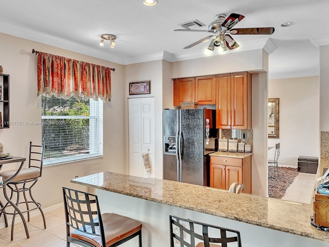 kitchen featuring light stone counters, a peninsula, a breakfast bar area, and black fridge