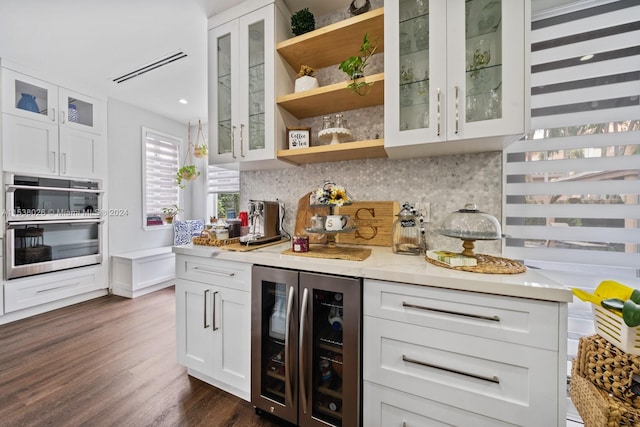 bar featuring stainless steel double oven, beverage cooler, tasteful backsplash, and white cabinetry