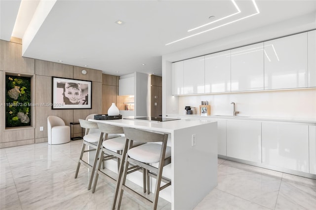 kitchen with light tile floors, a kitchen island, a breakfast bar area, black electric cooktop, and white cabinetry