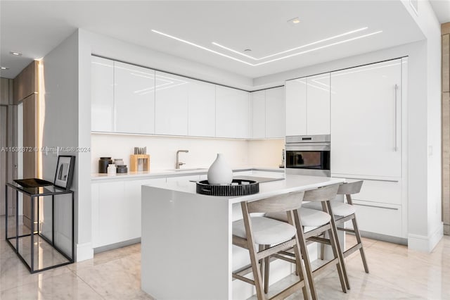 kitchen featuring white cabinets, stainless steel oven, a center island, and a breakfast bar