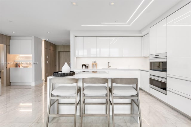 kitchen featuring stainless steel double oven, a kitchen breakfast bar, light tile floors, white cabinets, and a center island