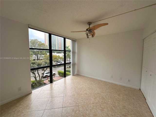 tiled spare room with expansive windows, ceiling fan, and a textured ceiling