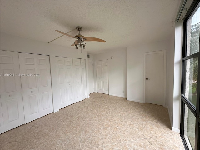 unfurnished bedroom featuring light tile floors, a textured ceiling, ceiling fan, and two closets