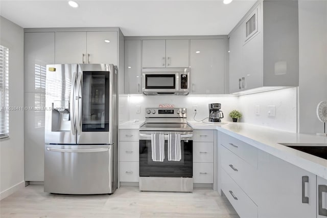 kitchen featuring gray cabinets, tasteful backsplash, appliances with stainless steel finishes, and light hardwood / wood-style floors