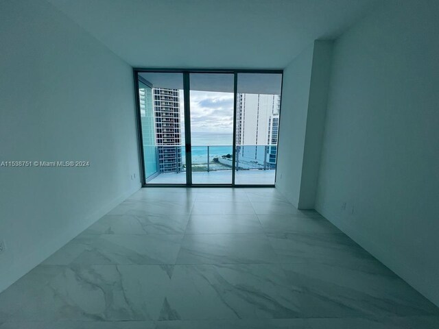 spare room with light tile floors, a water view, and a wall of windows