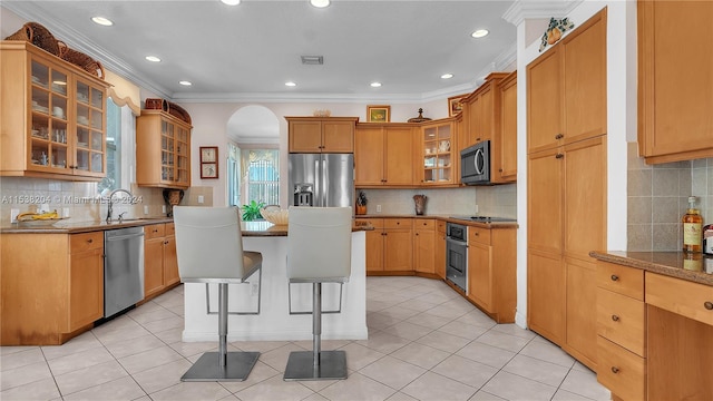 kitchen with light tile floors, ornamental molding, a breakfast bar area, appliances with stainless steel finishes, and backsplash