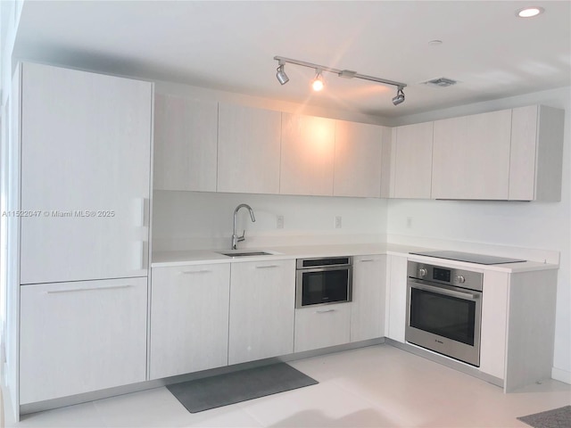 kitchen featuring black electric cooktop, rail lighting, oven, and sink