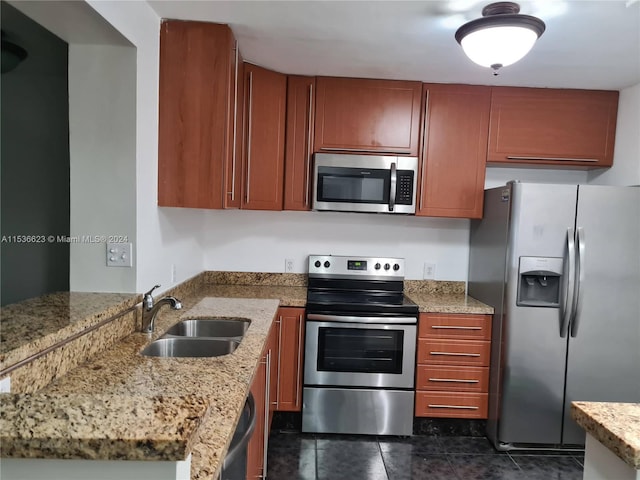 kitchen with dark tile flooring, light stone counters, appliances with stainless steel finishes, and sink