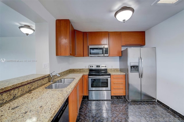 kitchen featuring appliances with stainless steel finishes, dark tile flooring, light stone countertops, and sink