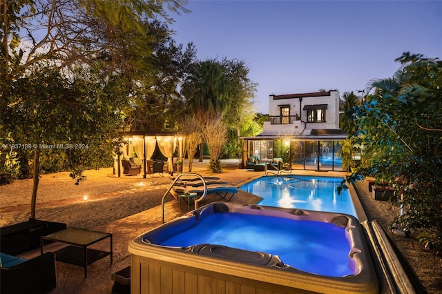 pool at dusk with a patio, an outdoor living space, and an in ground hot tub